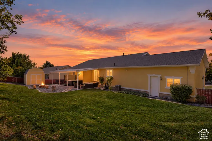 Backyard featuring a manicured lawn, stone-surfaced patio area, covered porch, and detached storage shed