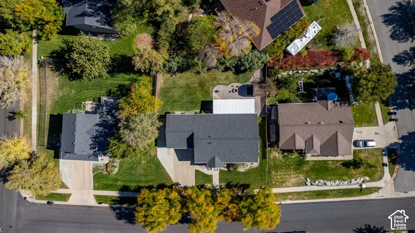 Aerial perspective of property featuring an expansive lawn, paved driveway, hardscaped patio area, and mature trees