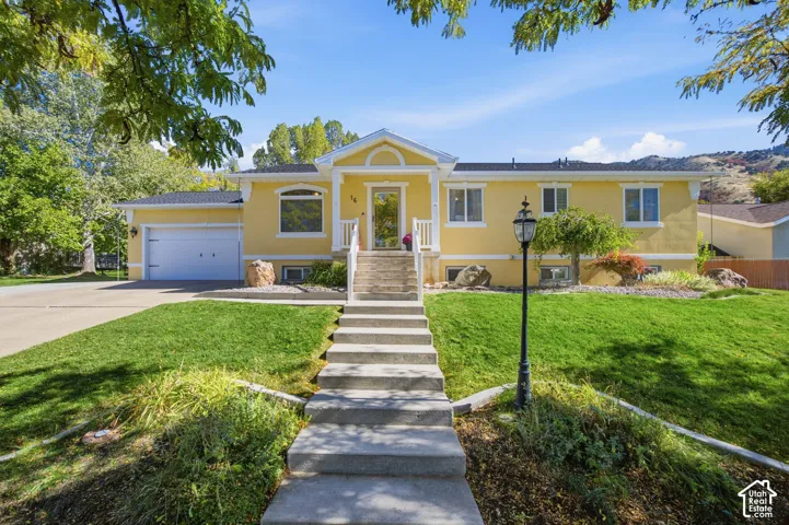 Single-story exterior featuring a stucco facade, front-facing attached garage, concrete staircase with white railings, and mountain backdrop
