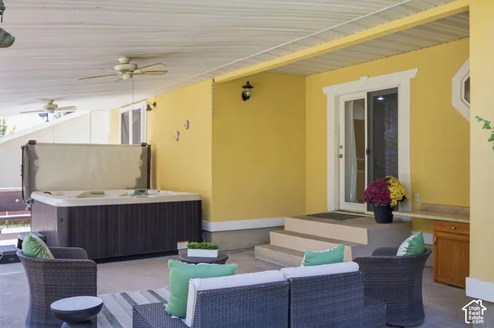 Covered patio featuring concrete flooring, dual ceiling fans, built-in hot tub, and exterior wall-mounted lighting
