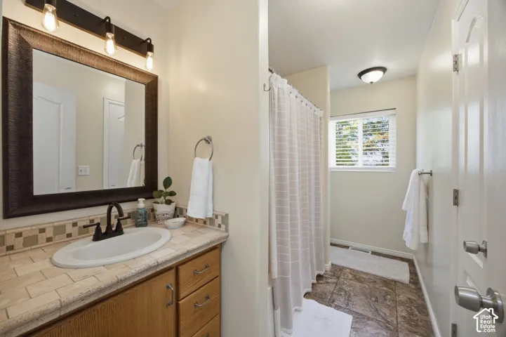 Bathroom featuring a wood-finish vanity with a tile countertop, an inset oval sink with a dark-toned faucet, a framed mirror with three-bulb vanity lighting, and tile flooring