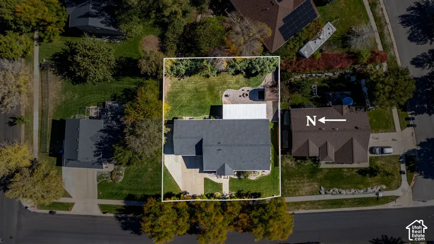 Aerial perspective featuring a shingled roof, concrete driveway, stone-paver patio, and lawn space