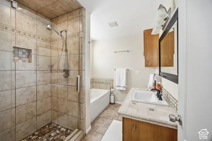 Walk-in shower with tile surround, stone-tiled floor, and recessed niche, accompanied by a soaking tub with decorative tile border and a vanity featuring a drop-in sink and stone-tiled countertop