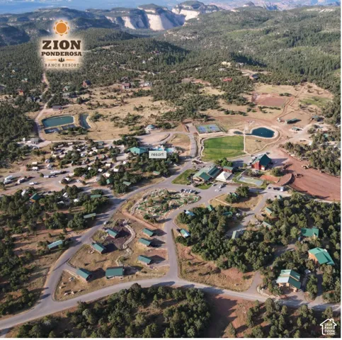 Aerial view of expansive ranch grounds featuring multiple structures, recreational ponds, tennis courts, and diverse pine tree terrain set against a mountainous backdrop