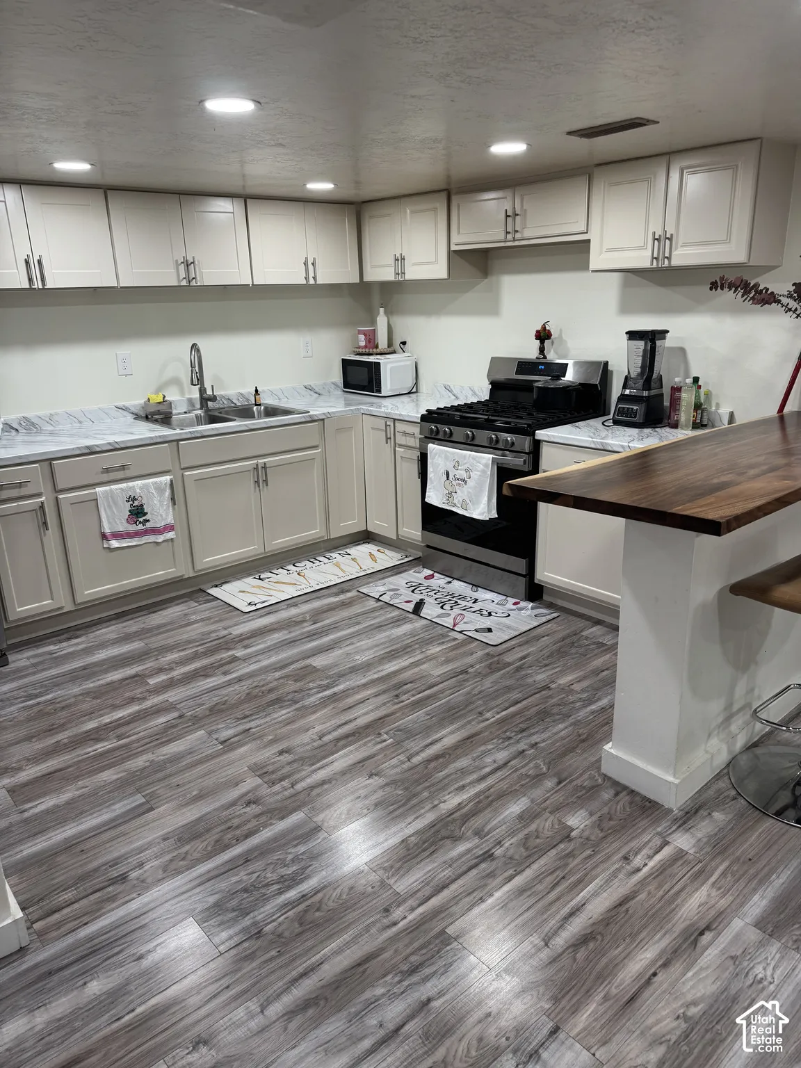 Kitchen featuring shaker-style cabinetry, patterned stone-finish countertops, wood-finish flooring, a stainless steel gas range, and a wood-top breakfast bar