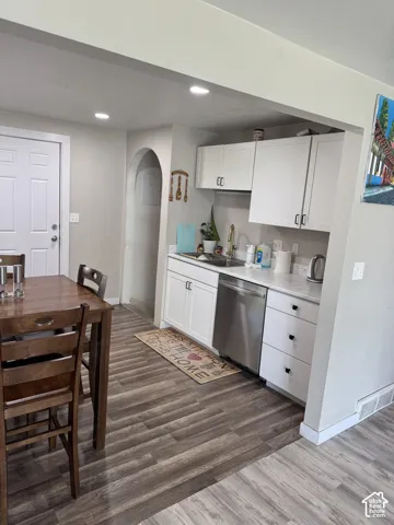 Kitchen featuring white cabinetry, wood-finish flooring, recessed lighting, a stainless steel dishwasher, and an arched entry to basement