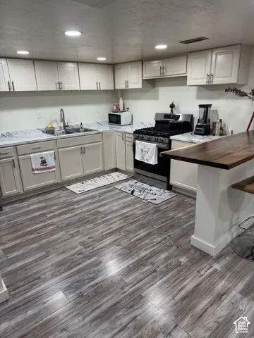 Kitchen featuring shaker-style cabinetry, patterned stone-finish countertops, wood-finish flooring, a stainless steel gas range, and a wood-top breakfast bar