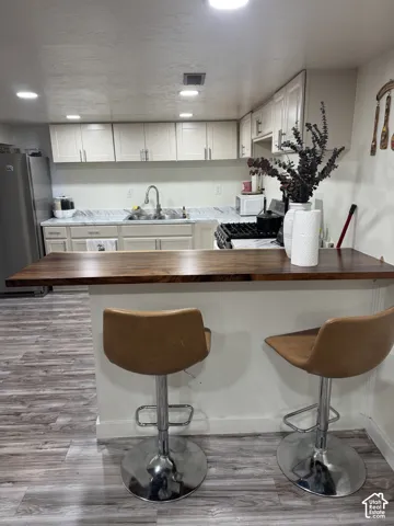 Kitchen featuring a natural wood-finish breakfast bar, light-toned cabinetry, patterned stone-finish countertops, stainless steel sink with a gooseneck faucet, and wood-finish flooring