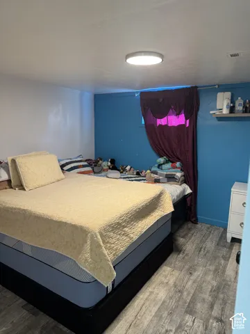 Room in basement with wood-finish flooring, accent wall, and ceiling-mounted flush light fixture