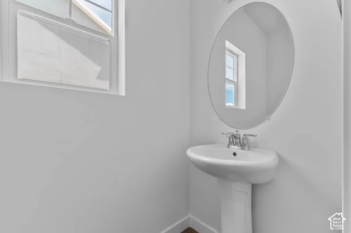 Pedestal sink featuring a polished chrome faucet, oval frameless mirror, and window with muntin detailing