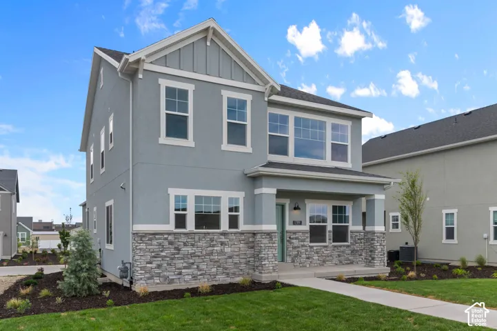 Two-story exterior featuring a mix of stucco and stone veneer siding, covered front porch with square columns, and multi-light windows