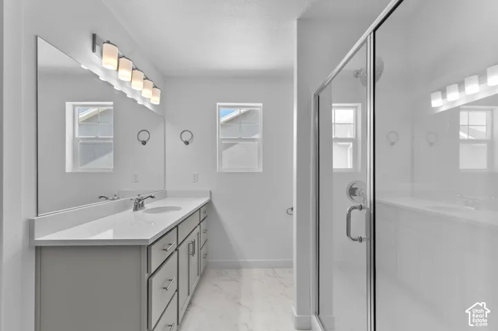 Bathroom featuring a dual-sink vanity with a quartz countertop, full-width mirror, multi-bulb vanity lighting, and a glass-enclosed shower