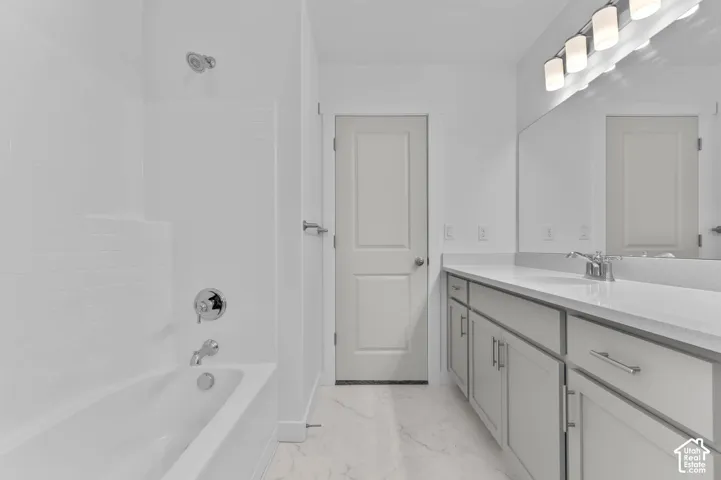 Bathroom featuring a white tub-shower combination, light gray vanity cabinetry with a stone countertop, oversized wall-mounted mirror, and multi-bulb vanity lighting