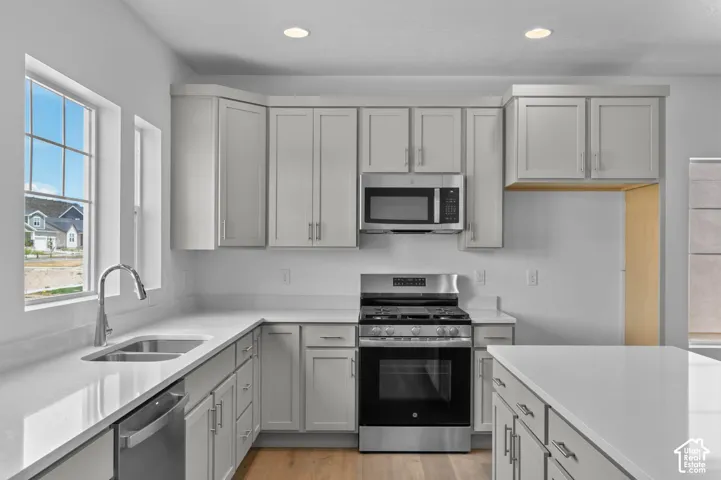 Kitchen featuring light grey Shaker-style cabinetry, white solid-surface countertops, stainless steel gas range, built-in microwave, and wood-finish flooring
