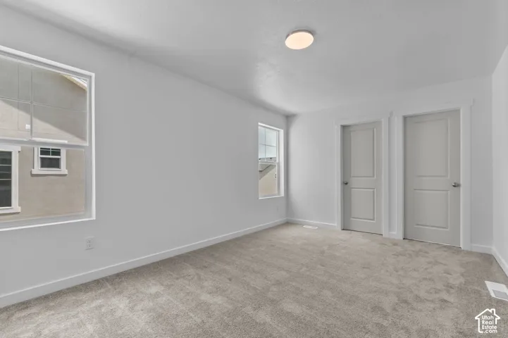 Room featuring neutral wall-to-wall carpeting, two multi-pane windows, dual interior doors with casing, and a flush-mount circular ceiling fixture