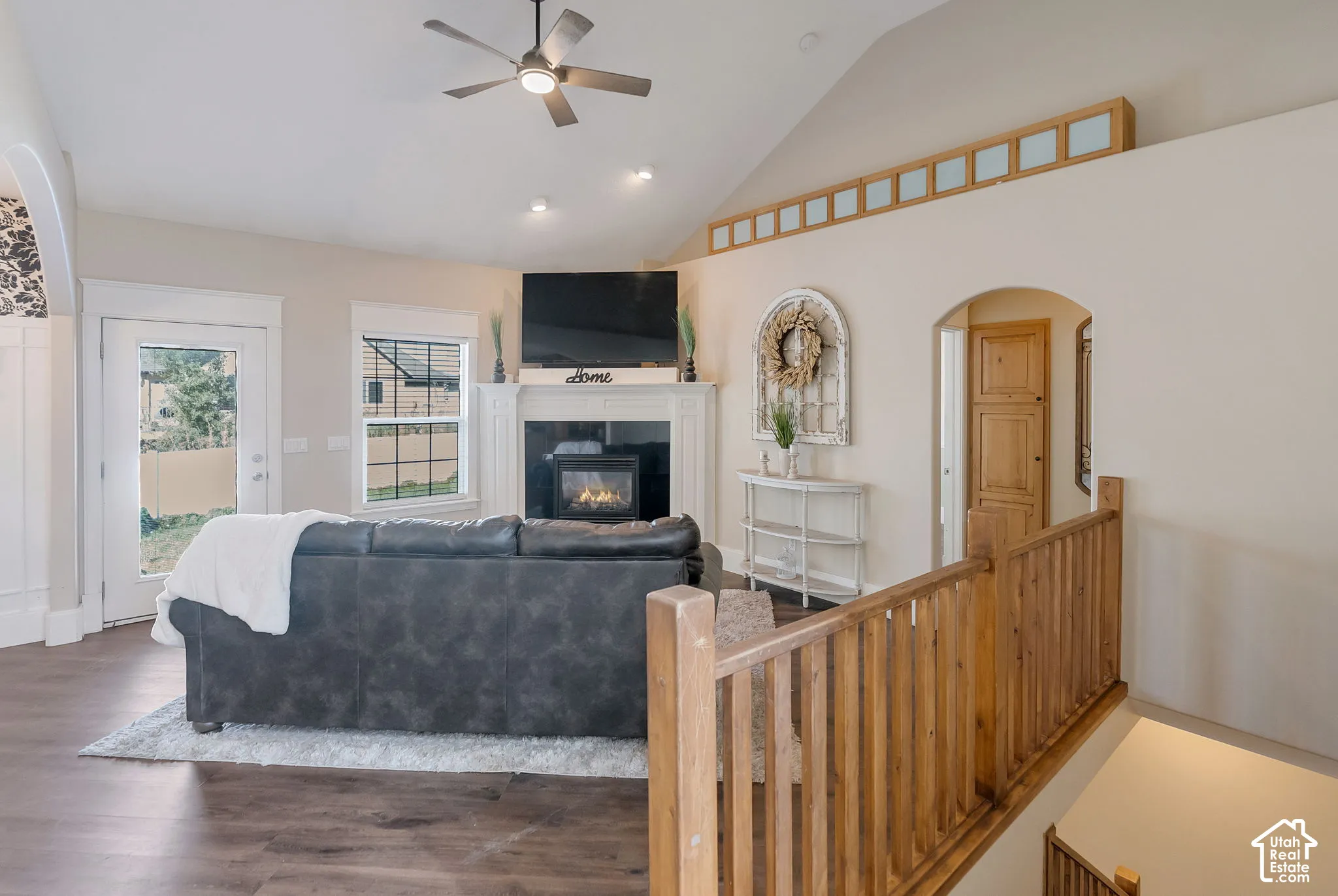 Vaulted ceiling featuring a central ceiling fan, fireplace with a white mantel, decorative transom windows, and wood-finish flooring