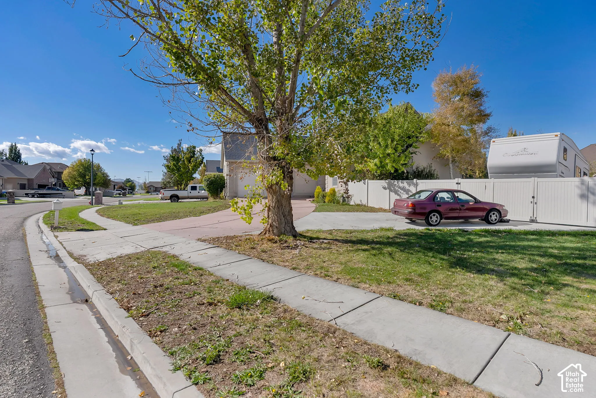 Corner lot property featuring concrete driveway, mature landscaping, and vinyl privacy fencing