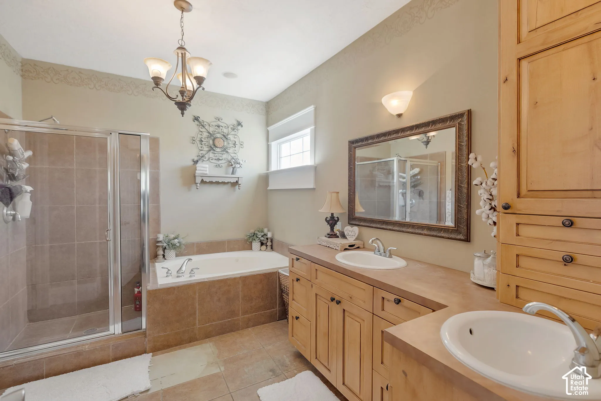 Bathroom featuring natural wood cabinetry, dual drop-in sinks, a separate soaking tub with tile surround, and a glass-enclosed shower