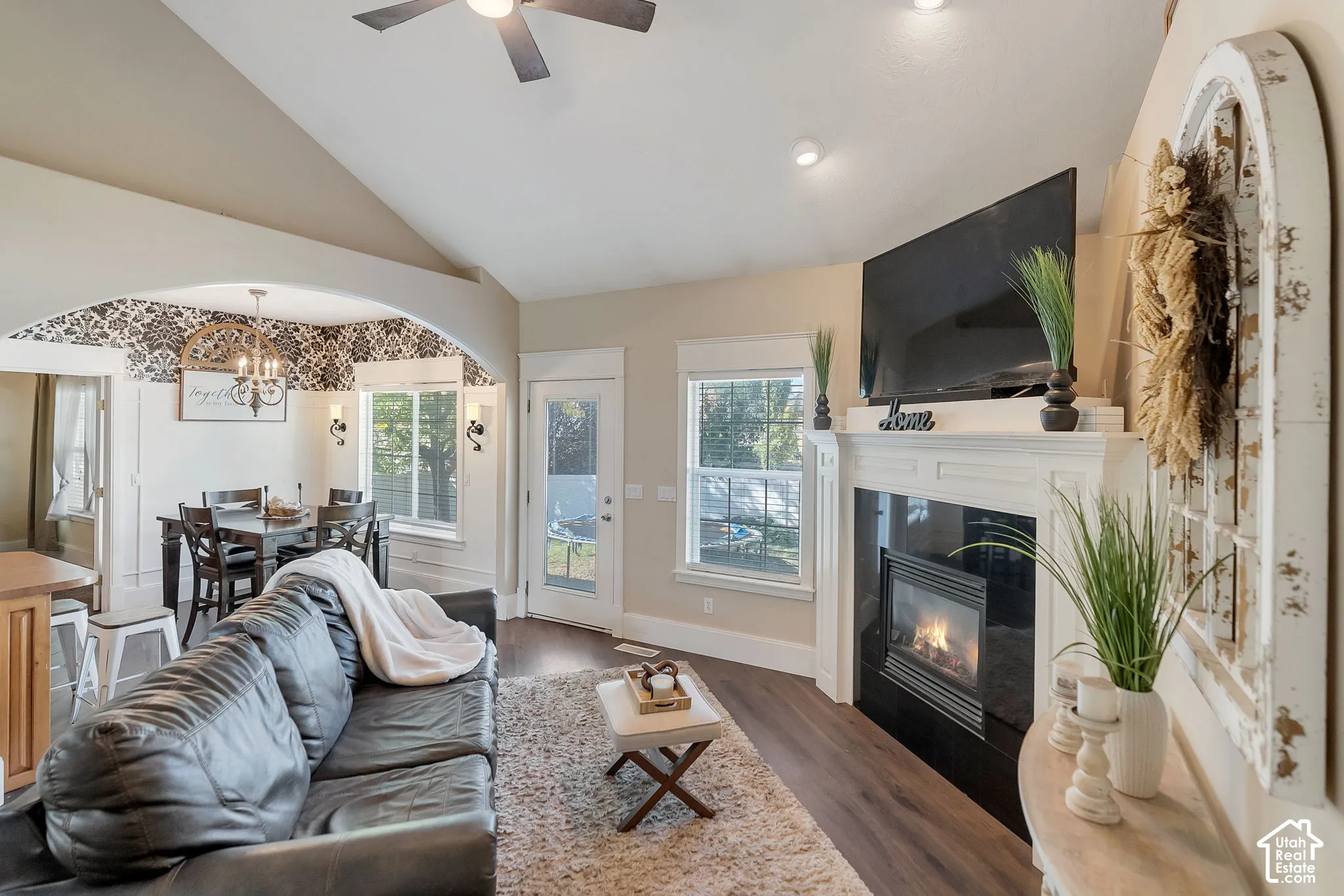 Living area featuring vaulted ceilings, wood-finish flooring, a fireplace with a decorative mantel, and an arched entry