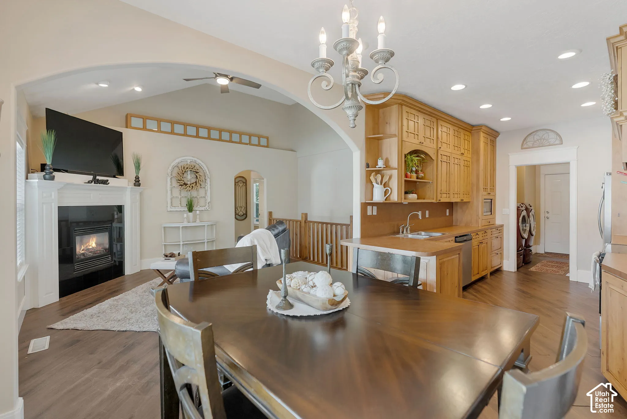 Vaulted ceilings with architectural archway, fireplace with white mantle, wood-finish flooring, custom wood cabinetry, and integrated lighting fixtures