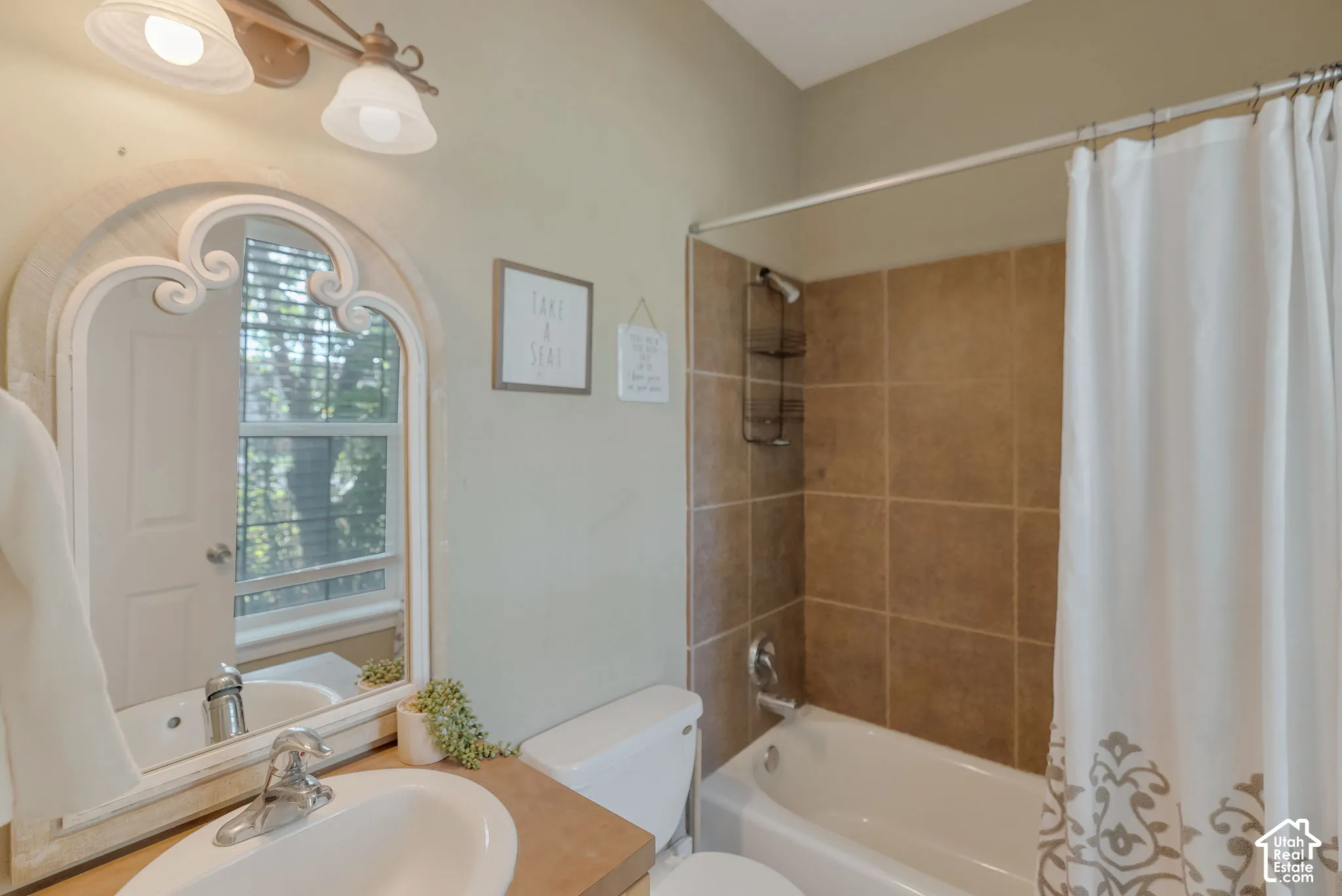 Bathroom featuring a vanity with an integrated sink, an arched decorative mirror, a dual-light fixture, and a tub-shower combination with floor-to-ceiling tile surround