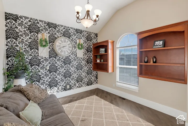 Vaulted ceiling featuring a central five-light chandelier, arched window, built-in wooden shelving, and patterned accent wall