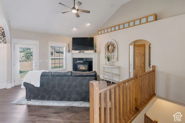 Vaulted ceiling featuring a central ceiling fan, fireplace with a white mantel, decorative transom windows, and wood-finish flooring