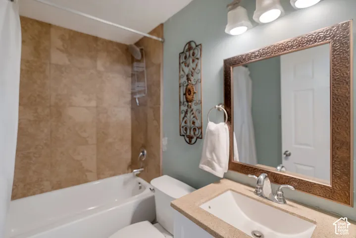 Bathroom featuring a tub-shower combination with floor-to-ceiling tile surround, stone-composite vanity countertop, integrated sink, and decorative framed mirror