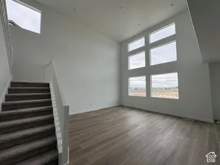 Double-height ceilings, expansive window configuration, wood-finish flooring, staircase with a white railing, and recessed lighting