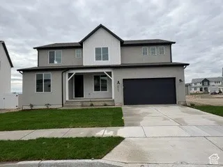 Two-story exterior featuring a neutral-toned stucco finish, vertical siding accents, a covered front porch with decorative brackets, and an attached two-car garage