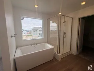Freestanding rectangular soaking tub with deck-mounted faucet, corner glass-enclosed shower, recessed lighting, and wood-finish flooring