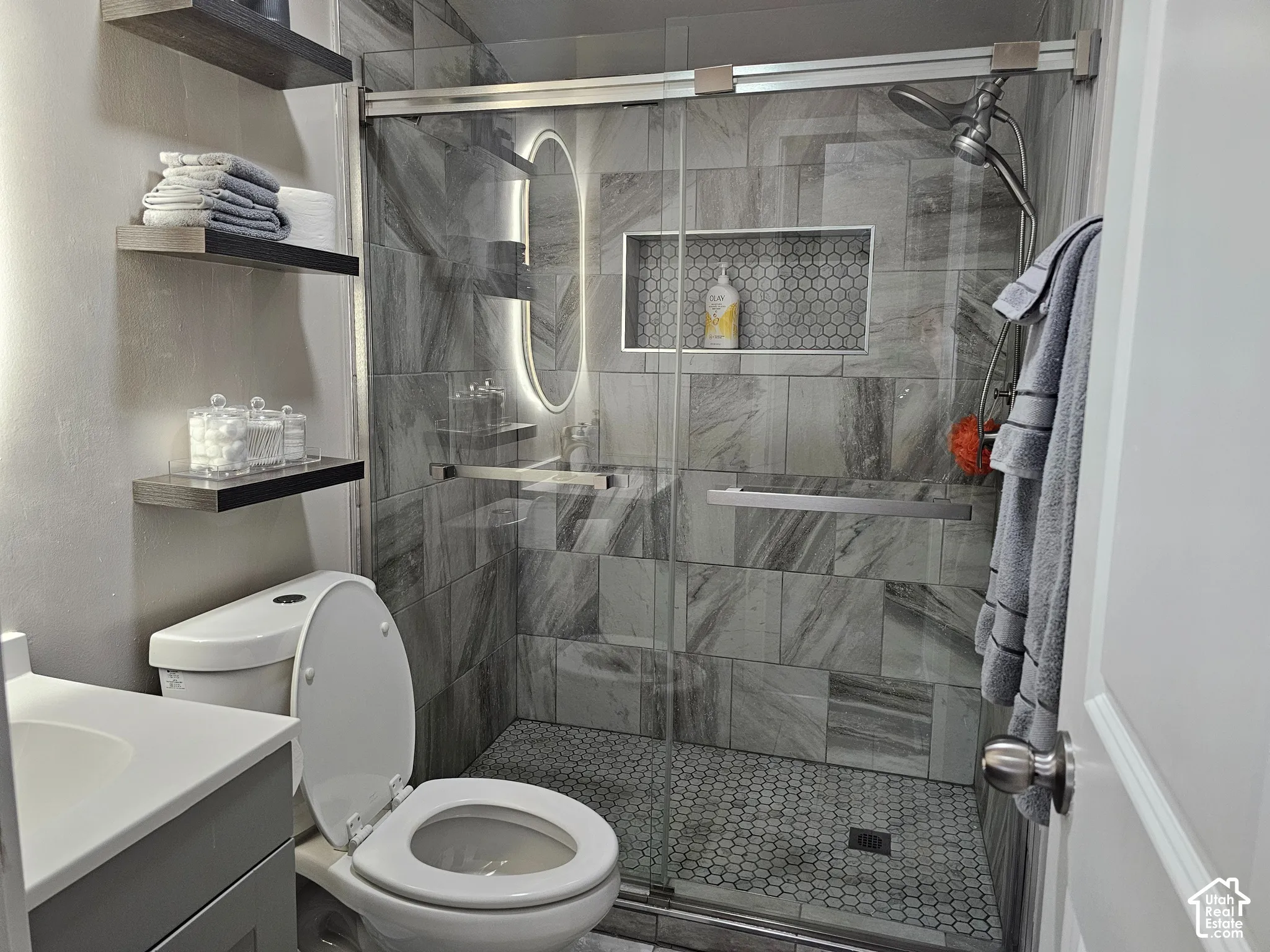Walk-in shower featuring large-format wall tile, a hexagonal mosaic tile floor, an integrated wall niche, and a glass sliding door