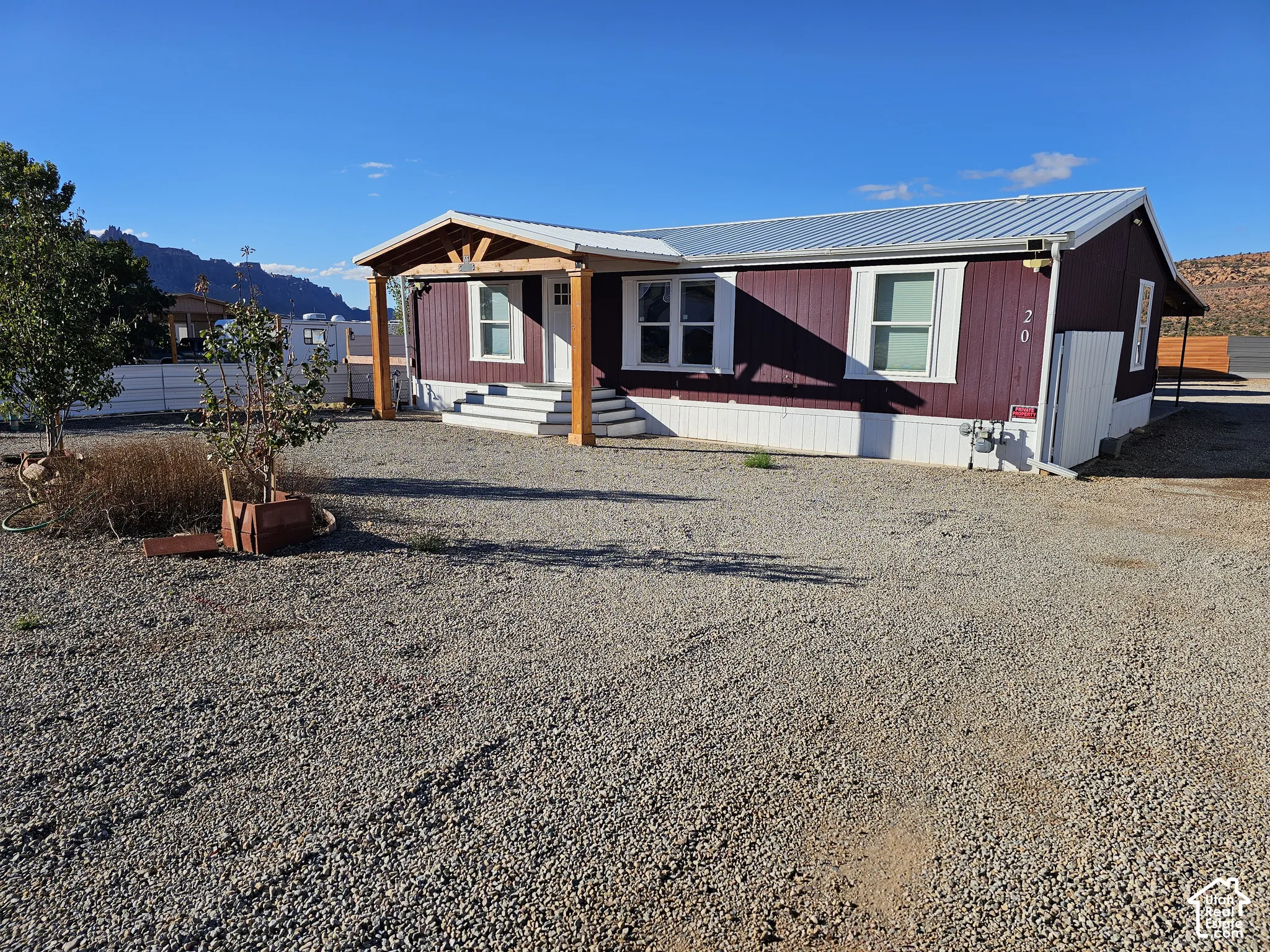 Single-level home featuring dark-toned vertical siding, a metal roof, a covered front porch with timber-frame support posts, and gravel surfacing