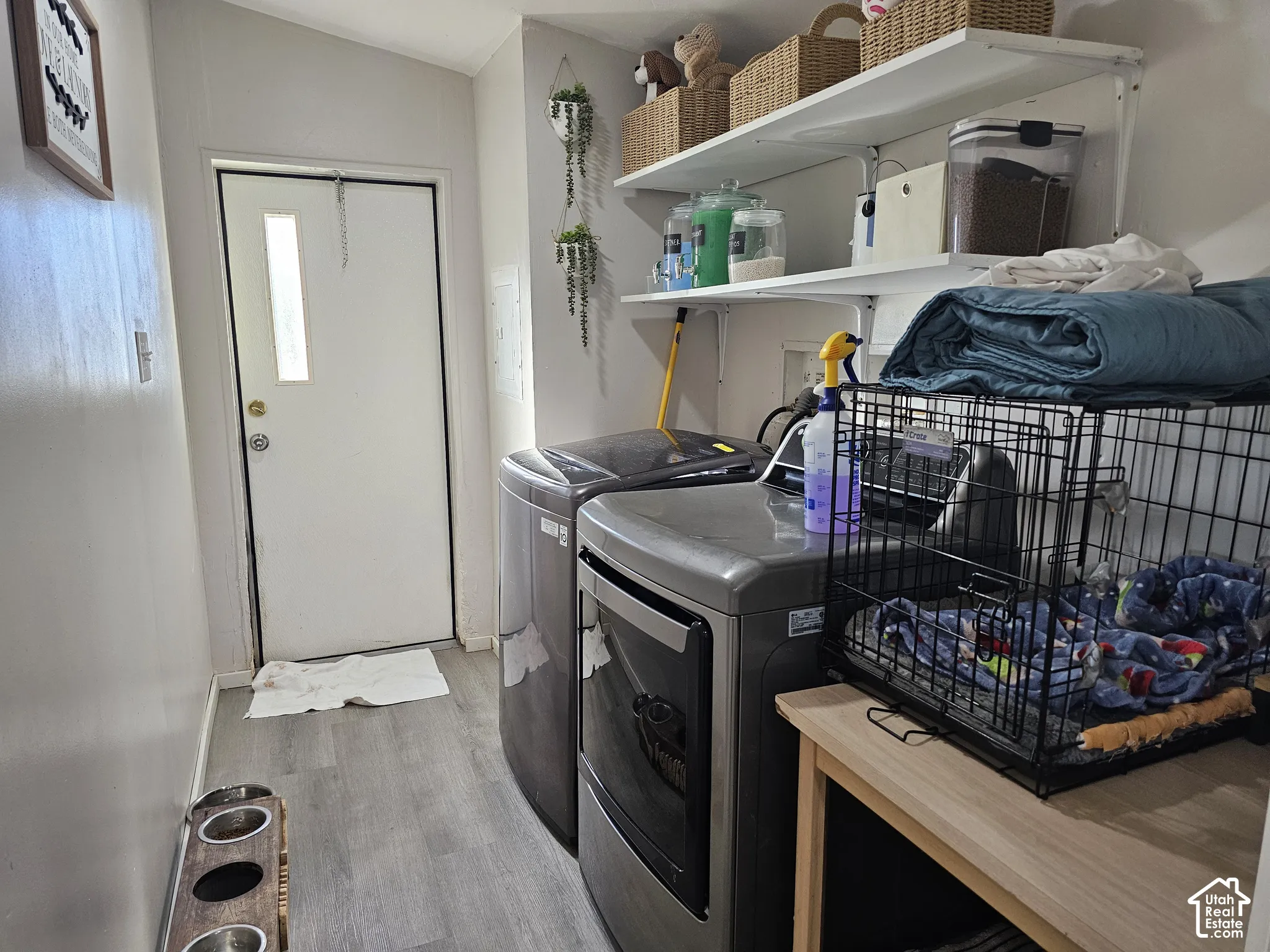 Utility space featuring wood-finish flooring, white wall-mounted open shelving, and an exterior door with a vertical glass insert