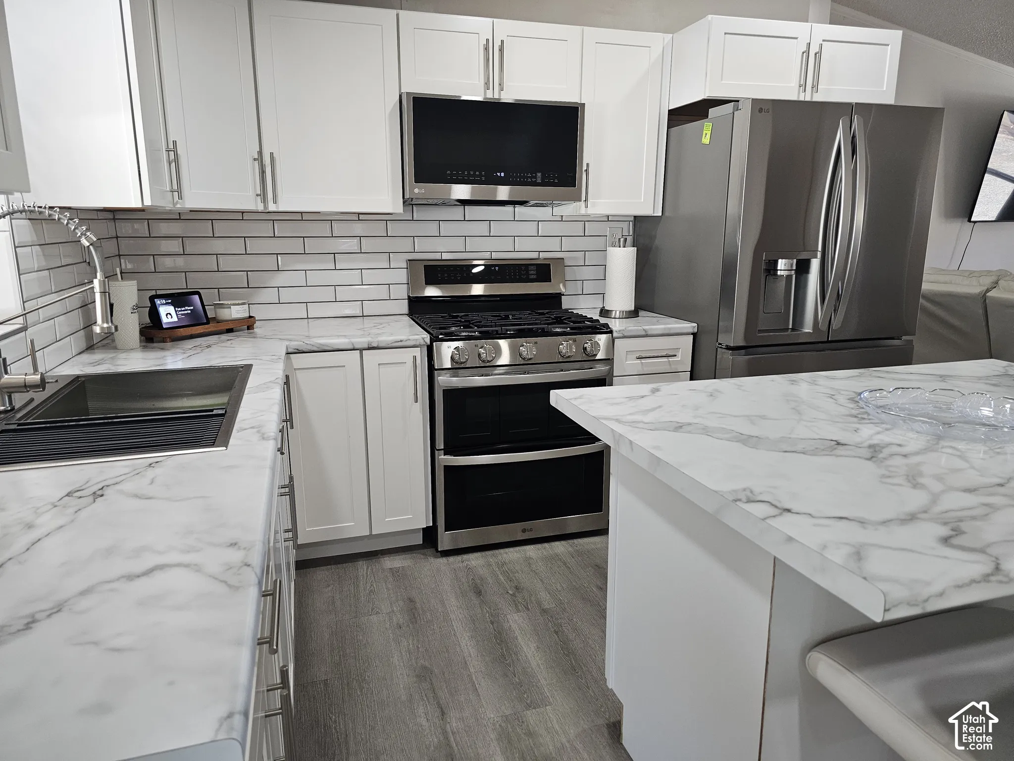 Kitchen featuring white shaker cabinetry, stone-patterned laminate countertops, stainless steel appliances, subway tile backsplash, and wood-finish flooring