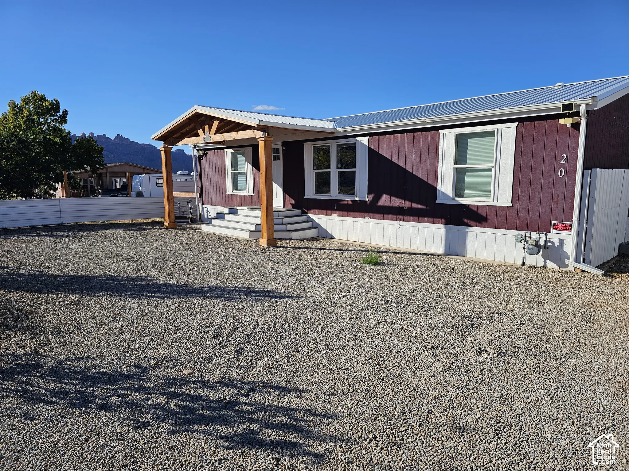 Exterior featuring vertical wood-style siding, metal roof, covered entryway with timber post support, and gravel-surfaced yard