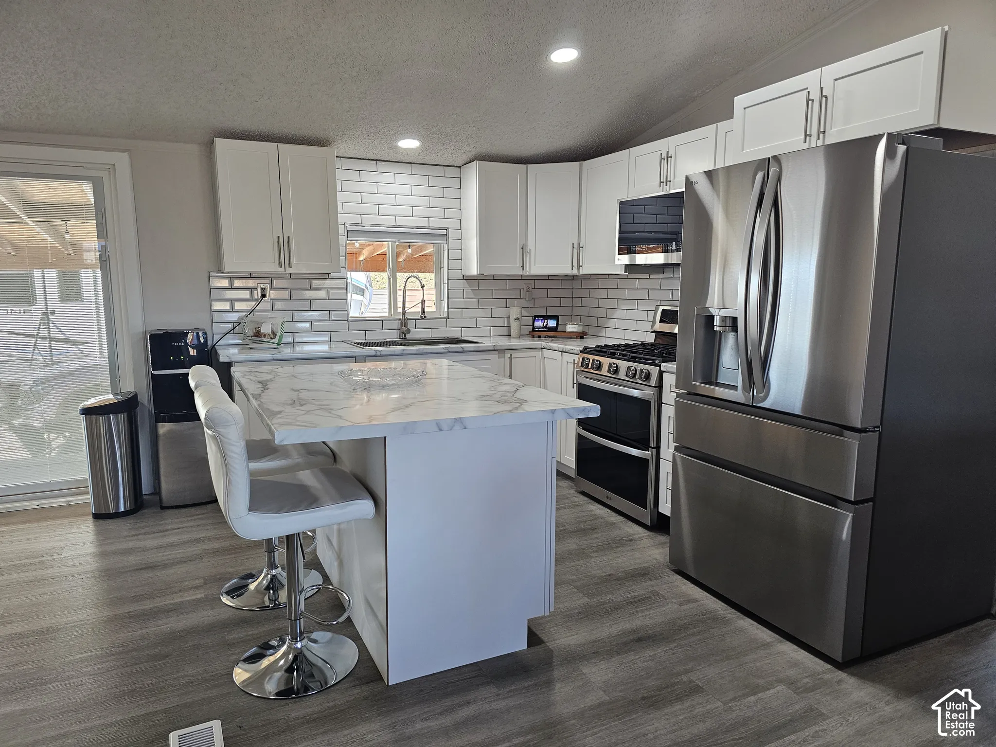 Kitchen featuring white cabinetry, stone-surface island, subway tile backsplash, wood-finish flooring, and stainless steel appliances