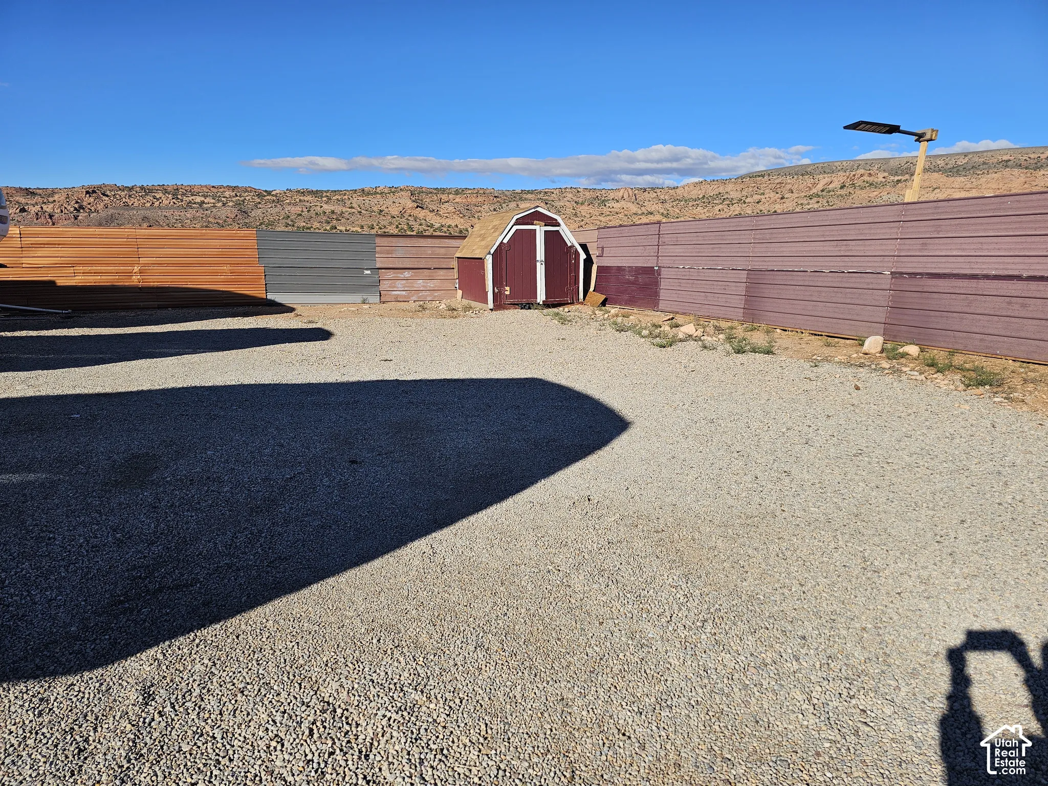 Gravel-surfaced exterior lot featuring a detached storage shed and corrugated metal perimeter fencing