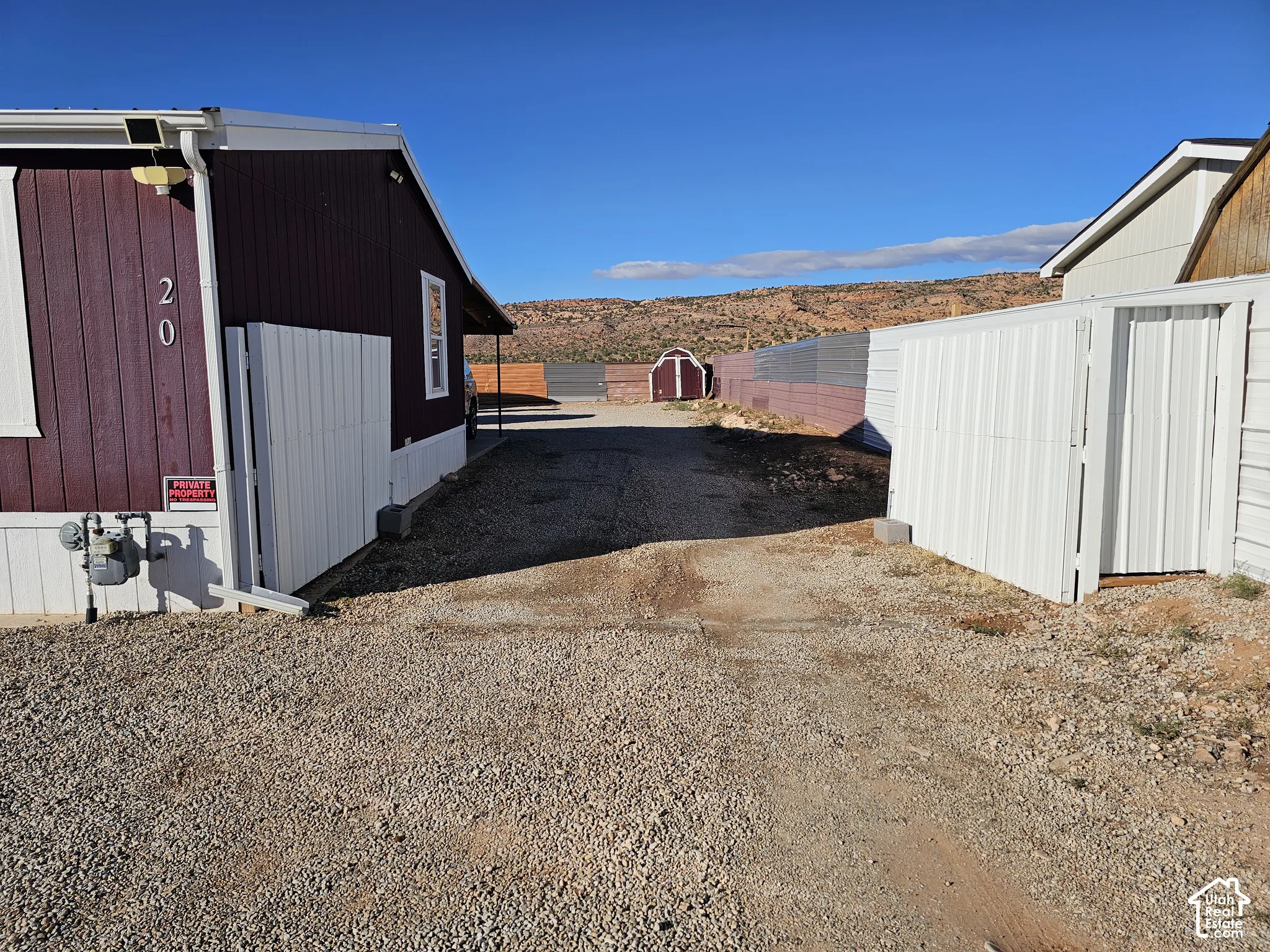 Gravel driveway featuring privacy fencing, exterior storage shed, and mountain scenery
