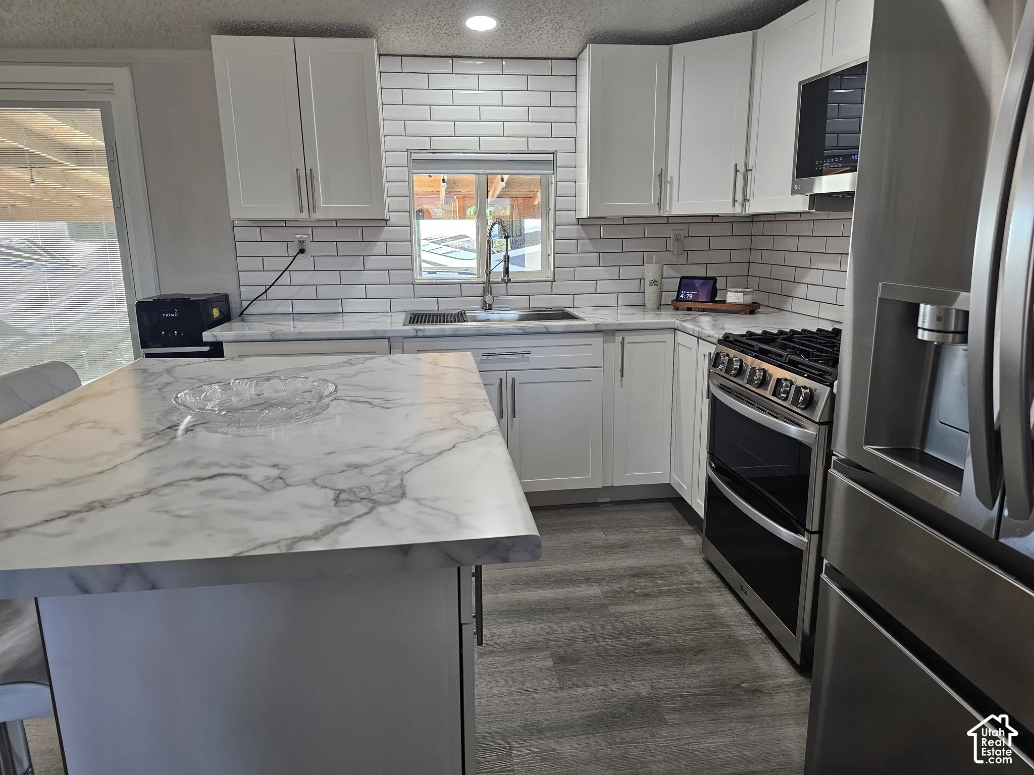 Kitchen featuring white cabinetry, subway tile backsplash, stone-finish countertops, stainless steel appliances, and wood-finish flooring