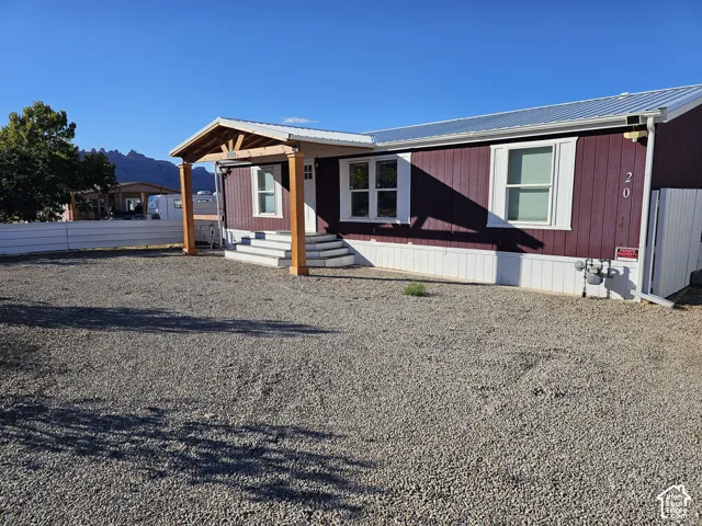 Exterior featuring vertical wood-style siding, metal roof, covered entryway with timber post support, and gravel-surfaced yard