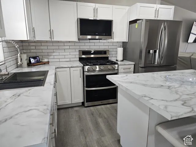 Kitchen featuring white shaker cabinetry, stone-patterned laminate countertops, stainless steel appliances, subway tile backsplash, and wood-finish flooring