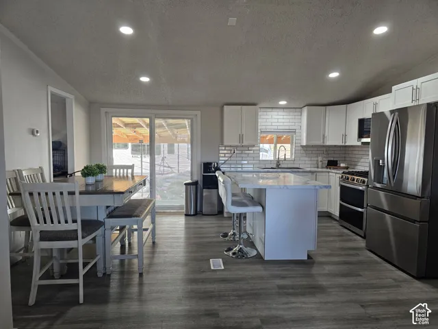 Kitchen featuring white cabinetry, an island with stone-finish countertop, stainless steel refrigerator and range, subway tile backsplash, and wood-finish flooring