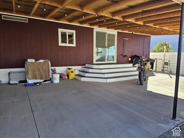 Covered concrete patio featuring an exposed timber beam ceiling, sliding glass entry door, and tiered exterior stairs