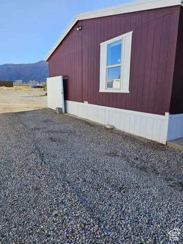 Exterior featuring vertical siding with a contrasting base skirt, single-pane window, wall-mounted light fixture, and gravel ground cover