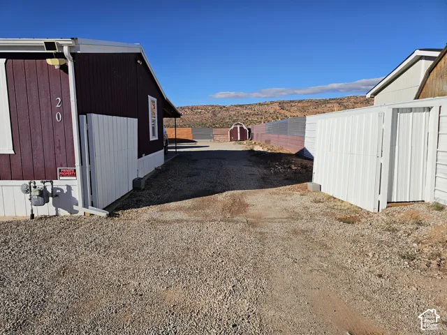 Gravel driveway featuring privacy fencing, exterior storage shed, and mountain scenery