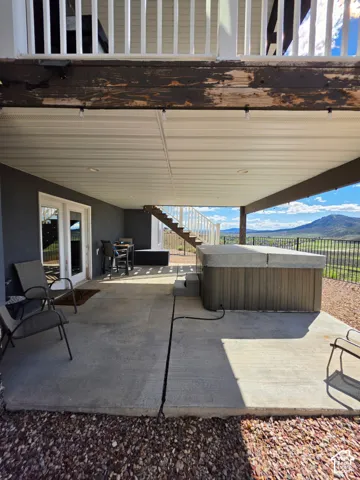 Covered concrete patio featuring recessed lighting, a built-in spa, metal railing, and mountain backdrop