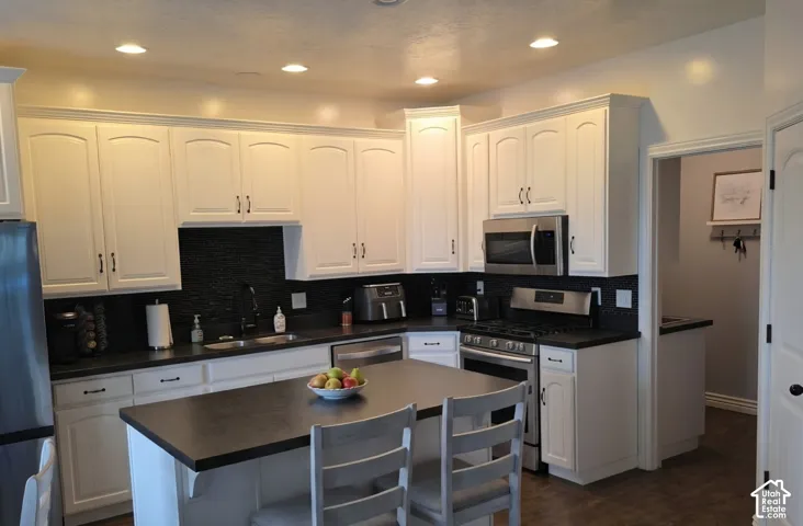 Kitchen featuring white cabinetry, dark countertops, a central island, recessed lighting, and stainless steel appliances