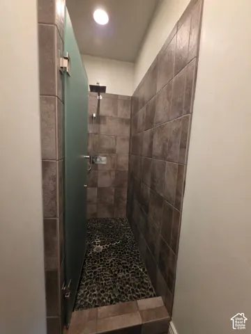 Walk-in shower featuring floor-to-ceiling tile surround, river stone floor detailing, a frosted glass door, and wall-mounted shower hardware