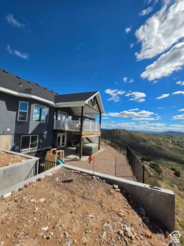 Exterior featuring a covered balcony with metal railing, tiered concrete retaining walls, gravel ground cover, and metal perimeter fencing